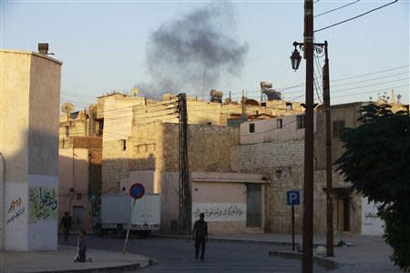 Smoke rises behind a Free Syrian Army fighter as he walks in Maysaloun neighborhood in Aleppo, October 27, 2013. REUTERS/Hamid Khatib