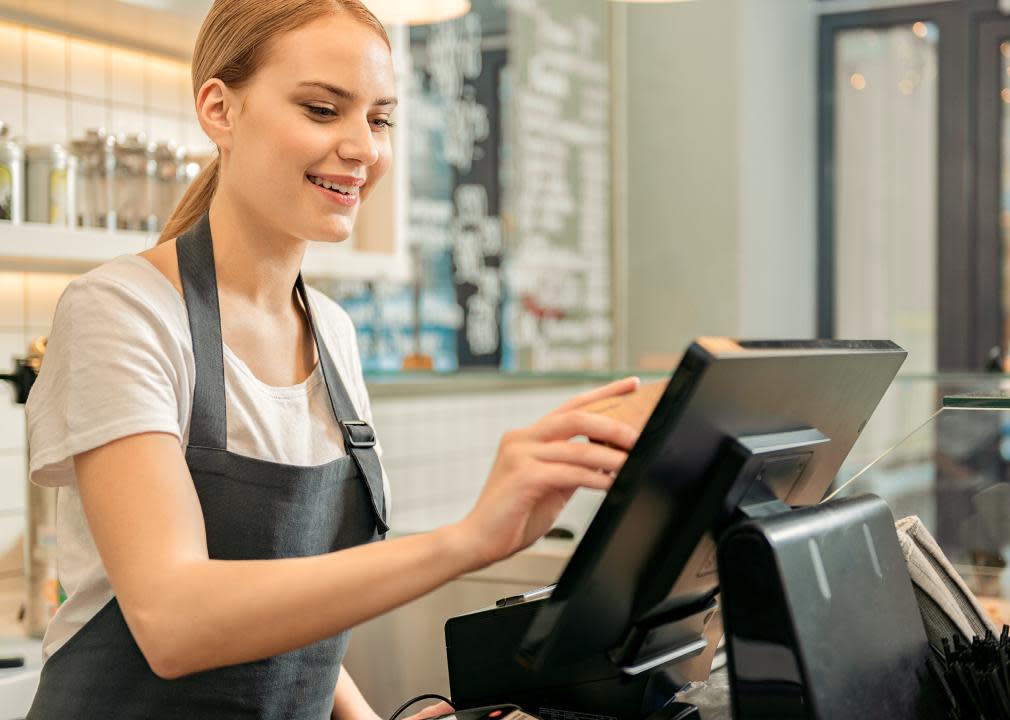 Cheerful cashier using a register for payment.