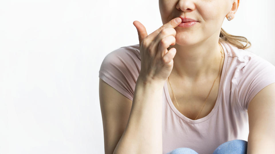 Red bubbles of virus herpes on lips of a woman in light pink t-shirt, lower part face is seen, which she touches with her finger. Medicine, treatment. White background. Horizontal with copy space