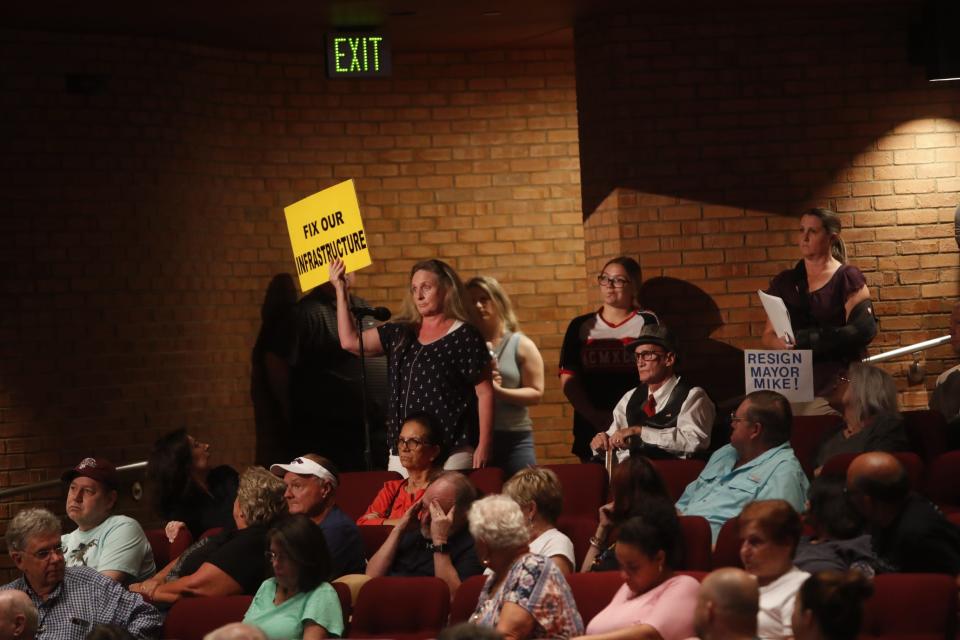 Germantown mayor Mike Palazzolo, along with other city leadership, hosts a town hall for Germantown residents in relation to the water crisis due to diesel leaking into a water reservoir on August 3, 2023 at the Germantown Performing Arts Center in Germantown, Tenn. A resident holds a sign that reads “fix our infrastructure” as she asks an array of questions to the panel.