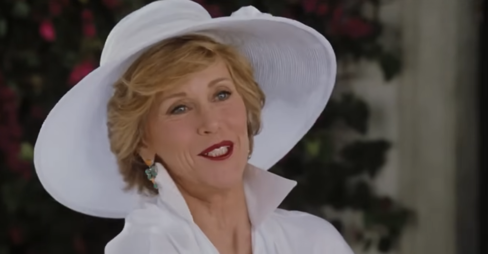 Jane Fonda wearing a wide-brimmed hat, white outfit, and teal earrings, smiling warmly