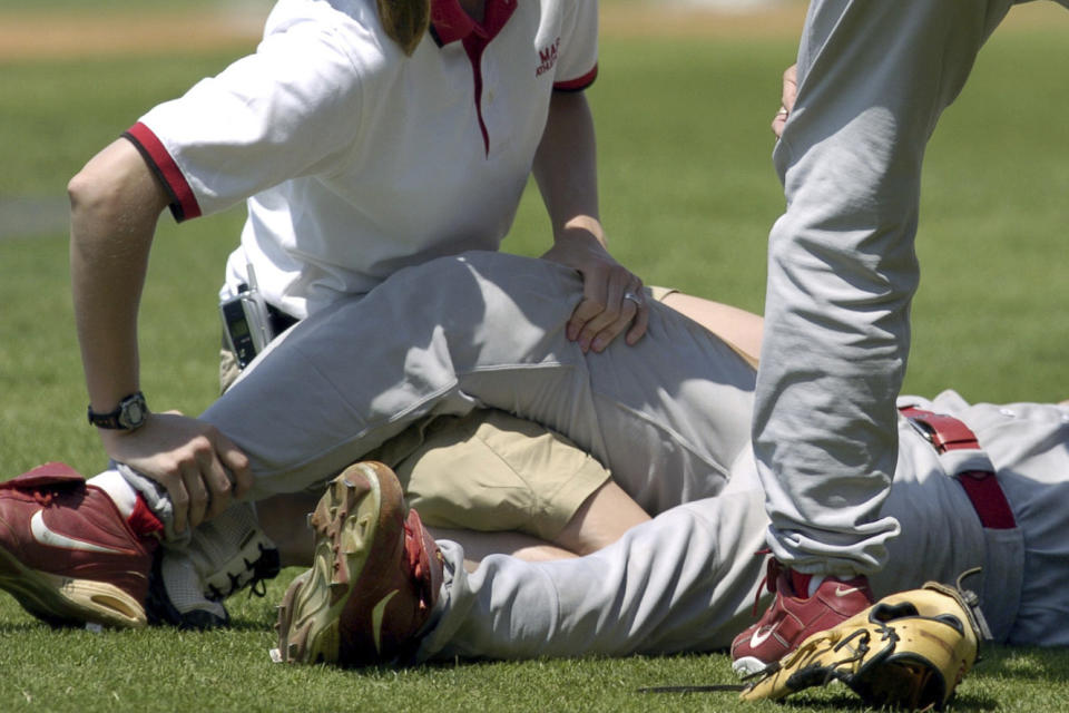FILE - A trainer works with Marist third baseman Pat Feeney (10) as he ground suffered cramping during an NCAA college baseball game against LSU in Baton Rouge, La., June 3, 2005. Colleges and universities are having a difficult time hiring, recruiting and retaining members of their athletic training staffs because of a number of below-market conditions, a survey shows. (AP Photo/Bill Feig, File)
