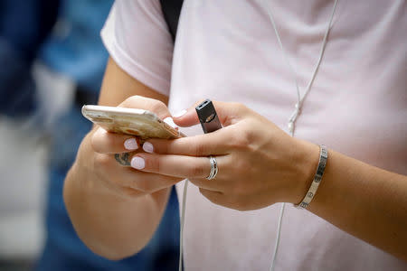 A woman holds a Juul e-cigarette as she uses her phone in New York City, U.S., September 13, 2018. REUTERS/Brendan McDermid