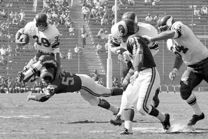 FILE - Minnesota Vikings halfback Hugh McElhenny, left, takes to the air to get past a Los Angeles Rams tackler during an NFL football game in Los Angeles, on Oct. 21, 1962. McElhenny, an elusive NFL running back nicknamed “The King,” died on June 17, 2022, at his home in Nevada, his son-in-law Chris Permann confirmed Thursday, June 23, 2022. He was 93. (AP Photo/Harold Filan, File)