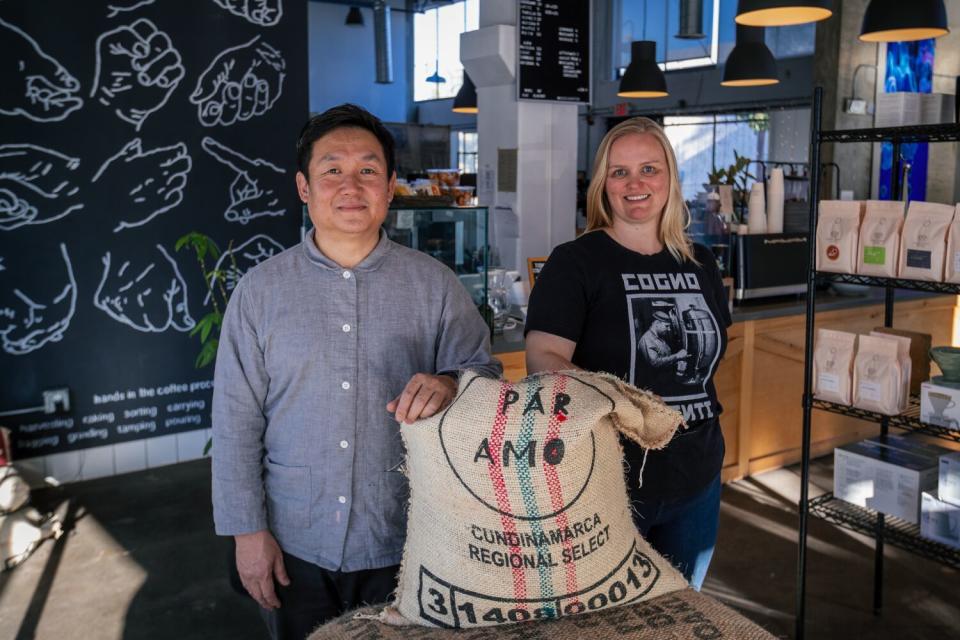 Two people in a coffee shop with a large burlap sack of coffee beans between them.