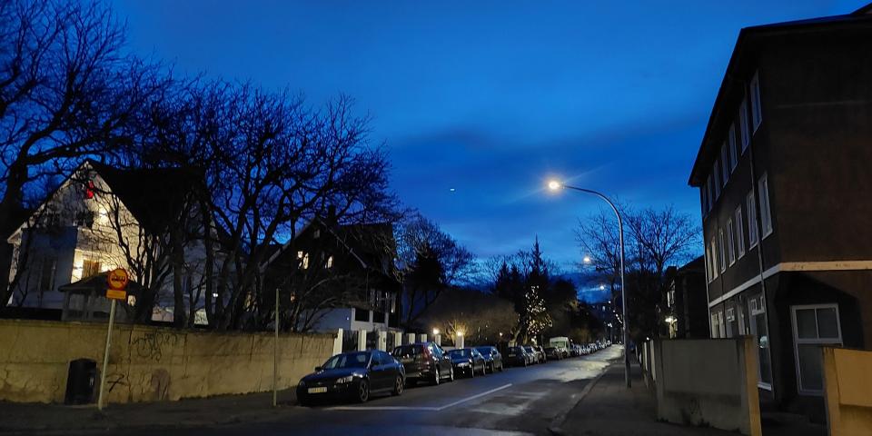 A photo showing a street in Reykjavik, Iceland with houses, cars and a streetlamp. Though it is the morning, the sky is still a very dark blue