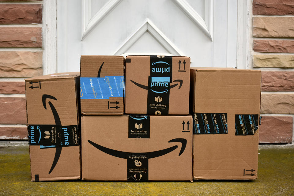 A picture of five cardboard boxes sitting on the porch before a white wooden door covered in the Amazon Prime logo and labels.