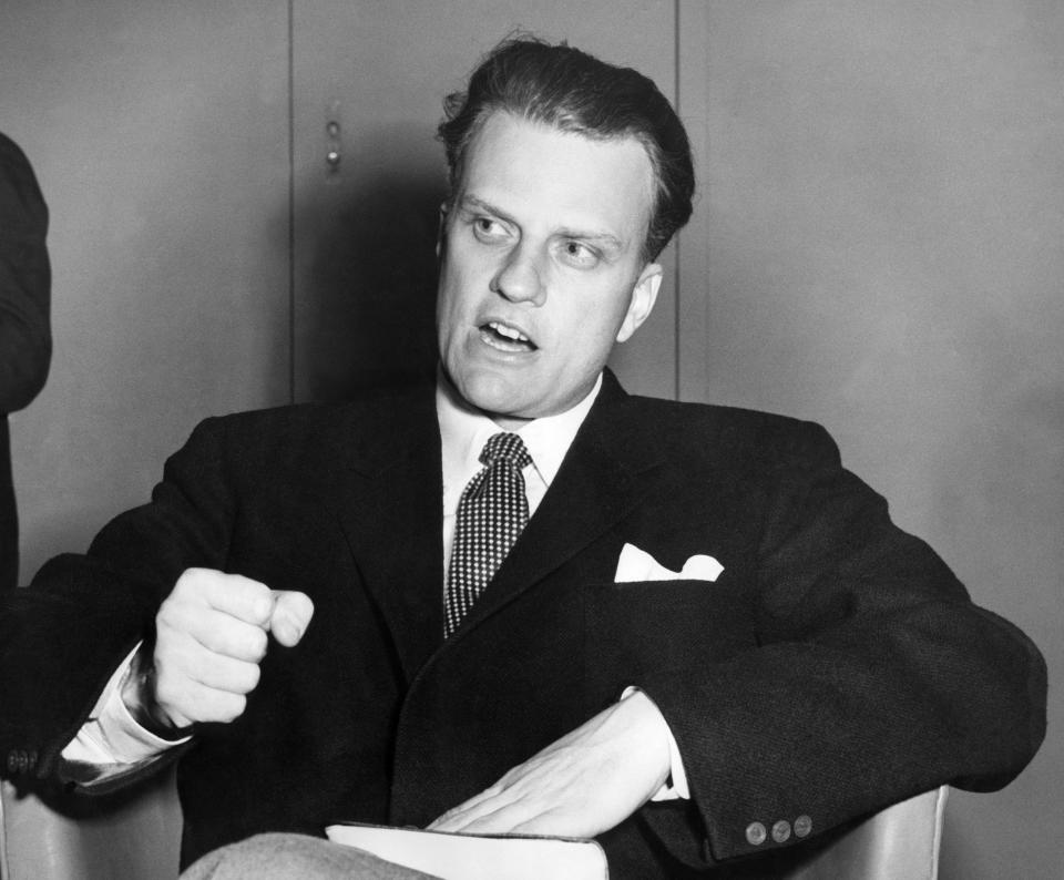 SOUTHAMPTON, UNITED KINGDOM:  Billy Graham, the American evangelist, the Bible beneath his hand, pounds his knee as he is interviewed aboard the liner 'United States' 26 February 1954 upon his arrival from New York to Southampton. Graham, (son of a dairy farmer, born in 1918 in Charlotte, NC), attended Florida Bible Institute and was ordained a Southern Baptist minister in 1939 and quickly gained a reputation as a preacher. During the 1950s he conducted a series of highly organized revivalist campaigns in the USA and UK, and later in South America, the USSR and Western Europe. (Photo credit should read AFP/Getty Images)