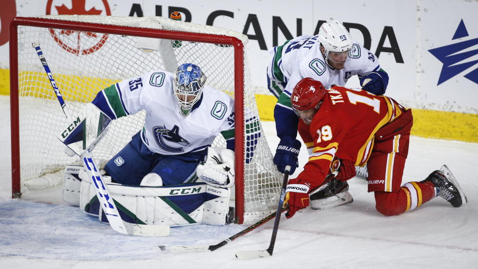 Vancouver Canucks' Bo Horvat, top right, checks Calgary Flames' Matthew Tkachuk, center, as Canucks goalie Thatcher Demko looks on during second-period NHL hockey game action in Calgary, Alberta, Monday, Jan. 18, 2021. (Jeff McIntosh/The Canadian Press via AP)