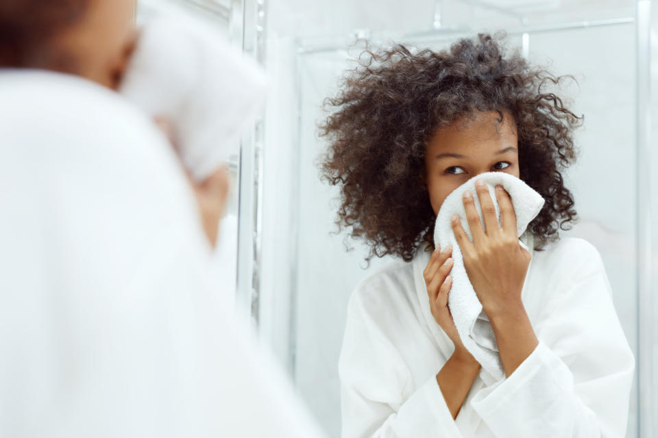 Washing face. Closeup of woman drying skin with towel looking in mirror at bathroom. Portrait of beautiful african girl wiping facial skin with soft facial towel