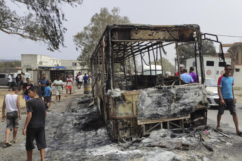 Residents walk past a charred truck in El Kala, in the El Tarf region, near the northern Algerian-Tunisian border, Thursday, Aug.18, 2022. Wildfires raging in the forests of eastern Algeria have killed at least 26 people, according to a "provisional report" by the north African country's interior minister. (AP Photo/Mohamed Ali)