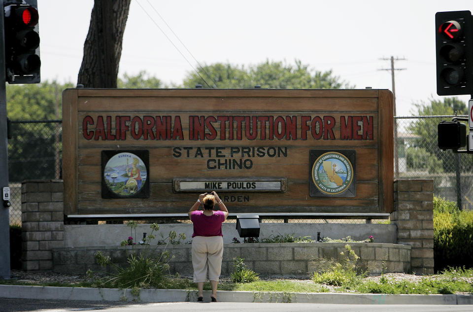 FILE - In this Aug. 9, 2009, file photo, a woman takes a photograph at the entrance of the California Institution For Men State Prison Chino, Calif. California lawmakers harshly criticized state corrections officials Wednesday, July 1, 2020, for a "failure of leadership" for botching their handling of the pandemic by inadvertently transferring infected inmates to an untouched prison, triggering the state's worst prison coronavirus outbreak. A third of the 3,500 inmates at San Quentin State Prison near San Francisco have tested positive since officials transferred 121 inmates from the heavily impacted California Institution for Men in Chino on May 30 without properly testing them for infections. (Ed Crisostomo/The Press-Enterprise via AP, File)