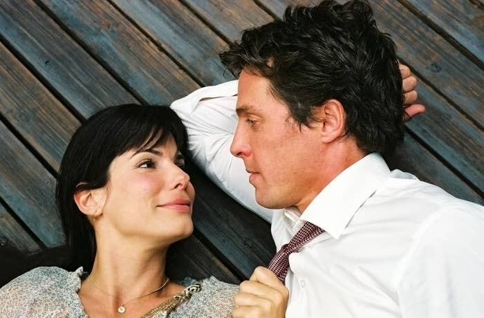 Two people lying on wooden floor, gazing at each other. The woman wears a light blouse, the man a white shirt and tie