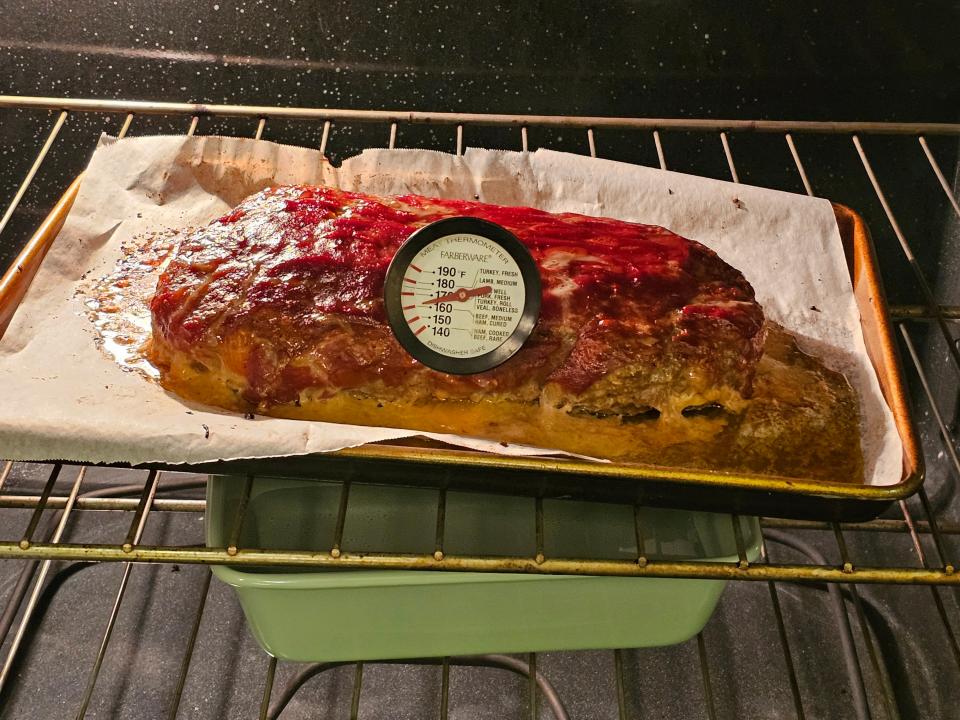 Meatloaf in oven with a meat thermometer sticking in it  and a pan of water below it