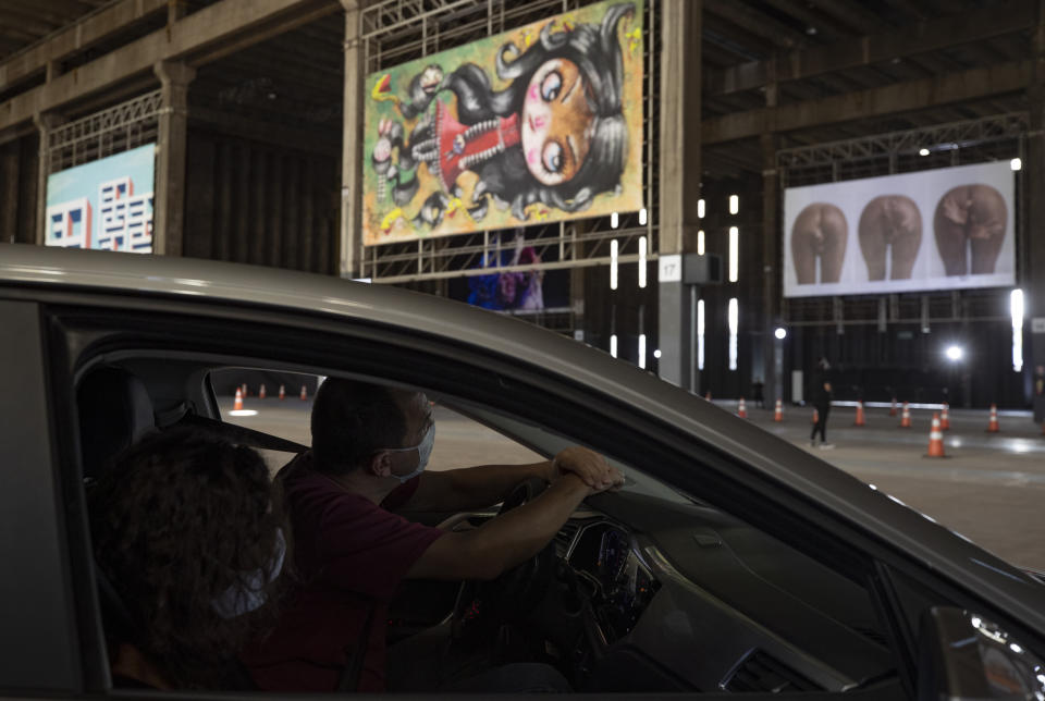 A man takes in an art exhibit from the inside of his car at a warehouse displaying paintings and photos in Sao Paulo, Brazil, Friday, July 24, 2020, amid the new coronavirus pandemic. Galleries, cinemas, theaters and museums are closed due to the restrictive measures to avoid the spread of COVID-19, but a group of artists and a curator found a way to overcome the restrictions to share their art with the residents of Brazil’s largest city. (AP Photo/Andre Penner)