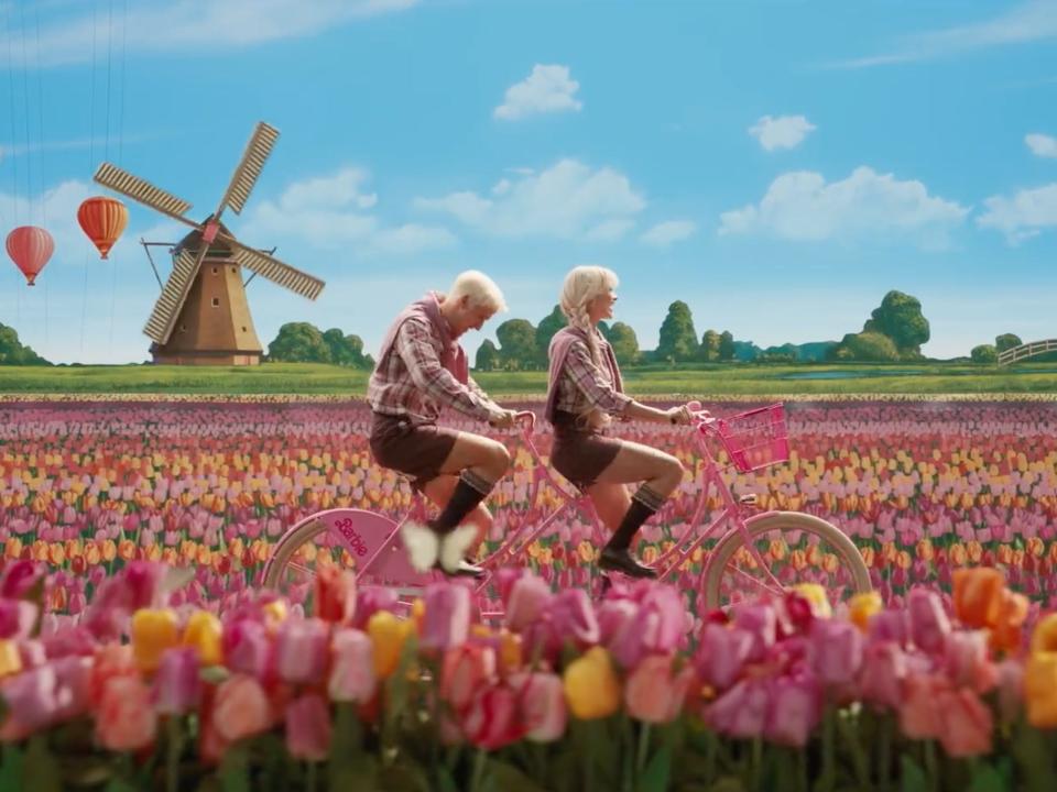 A scene from "Barbie" where Barbie and Ken are cycling through a field of tulips with a windmill in the background.