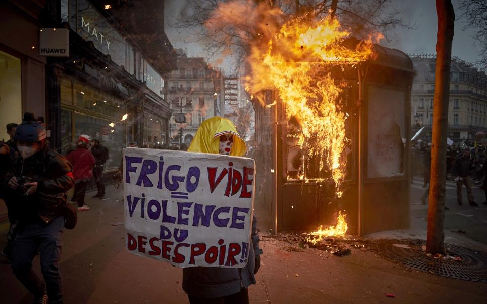 A protester holds a placard that reads "Empty Fridge equals Violence of Despair" in front of a burning news stand near Place de la Opera, Paris - Kiran Ridley/Getty Images