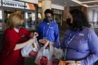 Volunteer Joan Kearl hands food to Wendy Haralson, right, and Amber Wilson outside a hotel Friday, March 26, 2021, in San Antonio. Kearl picked up the food for the quarantined Louisville women's basketball team participating in the NCAA tournament. The NCAA and local organizing groups set up expanded ambassador and item-delivery services relying on volunteer help to take care of needs for players, officials and others working inside. (AP Photo/Morry Gash)