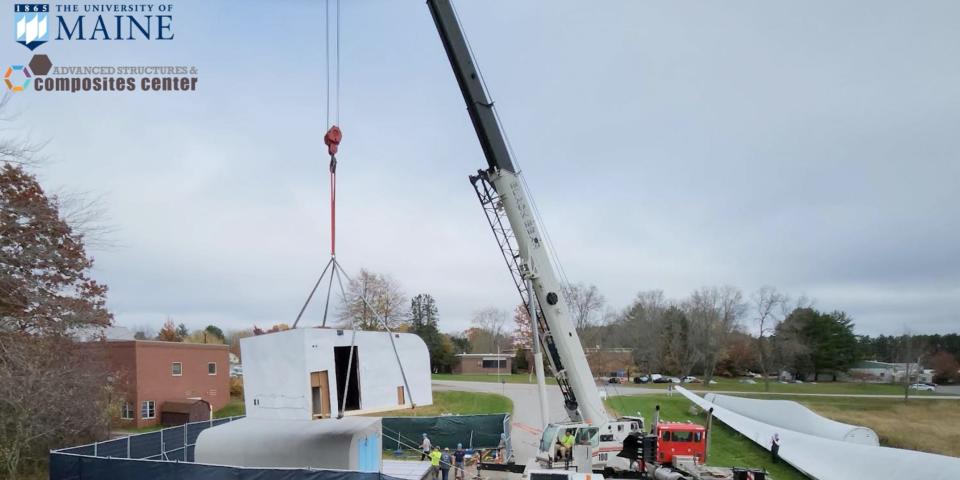 A module of University of Maine Advanced Structures and Composites Center's 3D printed tiny home being moved outside with a crane
