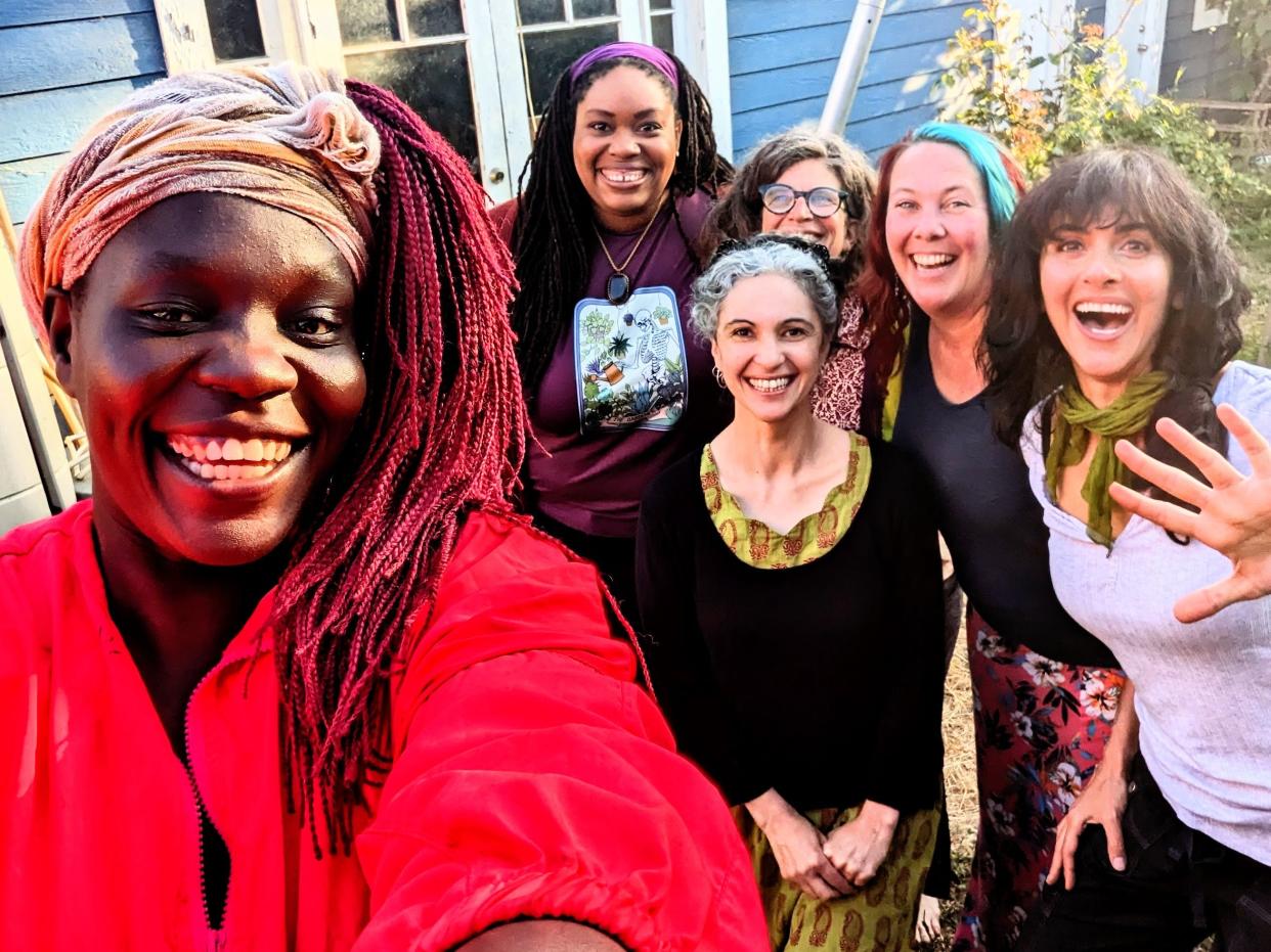 A photo of Ari Honarvar and her friends. One of her friends wears an orange scarf around her head. She has red-dyed braids, wears a red top and smiles widely. Behind her stand a group of women smiling at the camera