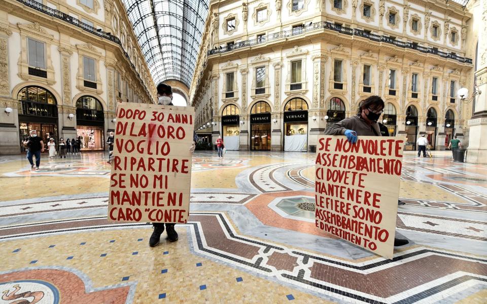 People hold banners as they take part in a protest at Galleria Vittorio Emanuele II, as Italy eases some of the lockdown measures put in place during the coronavirus disease - REUTERS