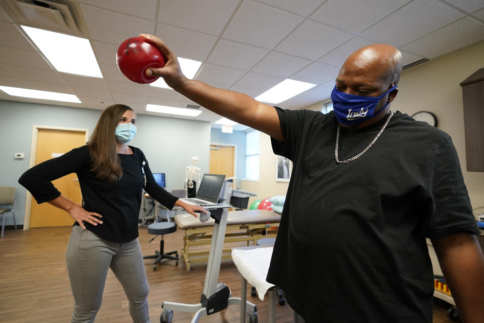 Emily Smith watches as Larry Brown lifts a weighted ball during an occupational therapy session at Community Health Network, Thursday, Aug. 20, 2020, in Indianapolis. He didn’t die of COVID-19, but he’s coming to terms with the fact that his life might never be the same. (AP Photo/Darron Cummings)