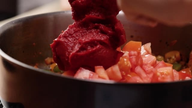 Adding tomato paste to tomatoes in frying pan