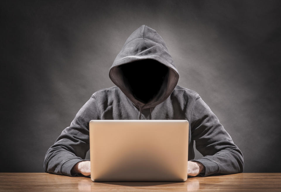 Hacker in a hoodie sitting with a laptop.