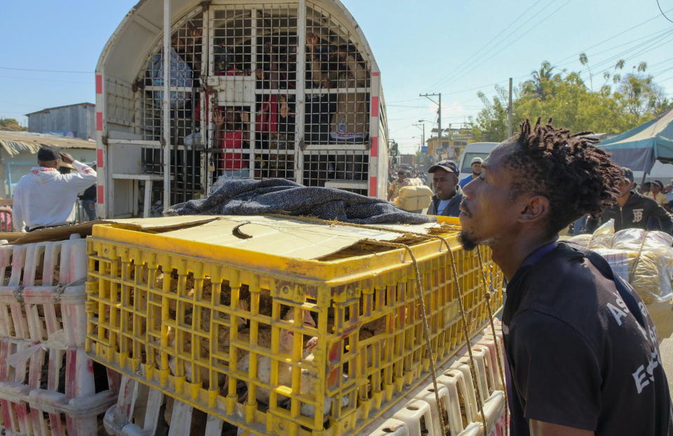 A vendor pushes crates of chickens past a police truck of people detained for deportation on the border bridge that connects Dajabon, Dominican Republic with Haiti, Monday, March 18, 2024. (AP Photo/Ricardo Hernandez)