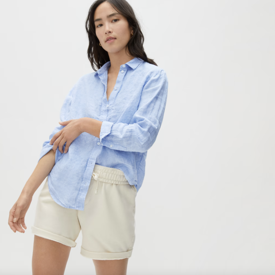 model with black hair in beige shorts and blue button down The Linen Relaxed Shirt (Photo via Everlane)