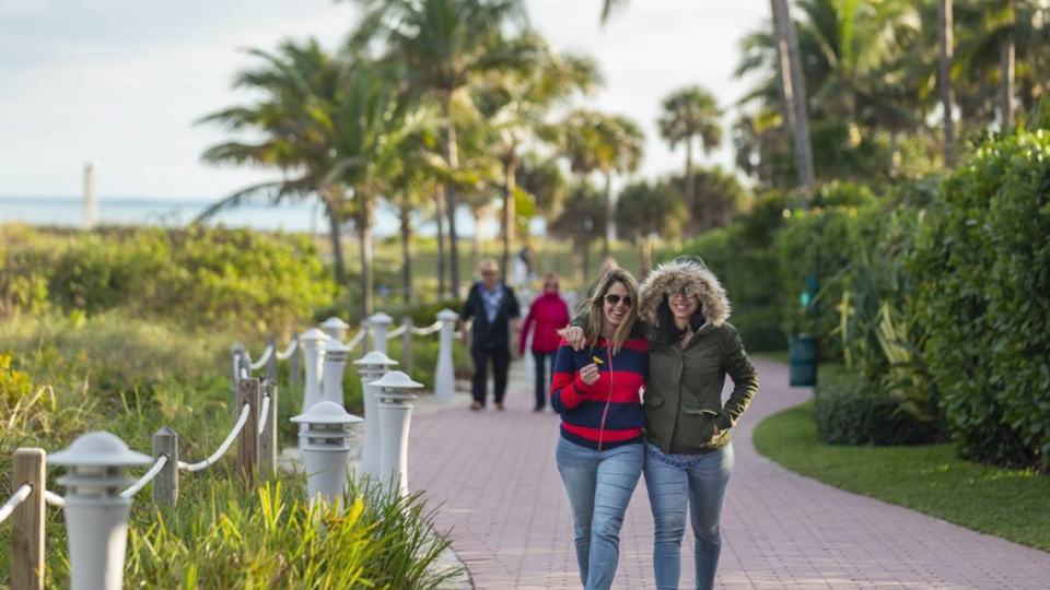 Regina Soares, izquierda, y Rafaela Squiabel, turistas de Boston, caminan cerca de South Pointe Park Pier en Miami Beach el lunes 28 de enero de 2019.