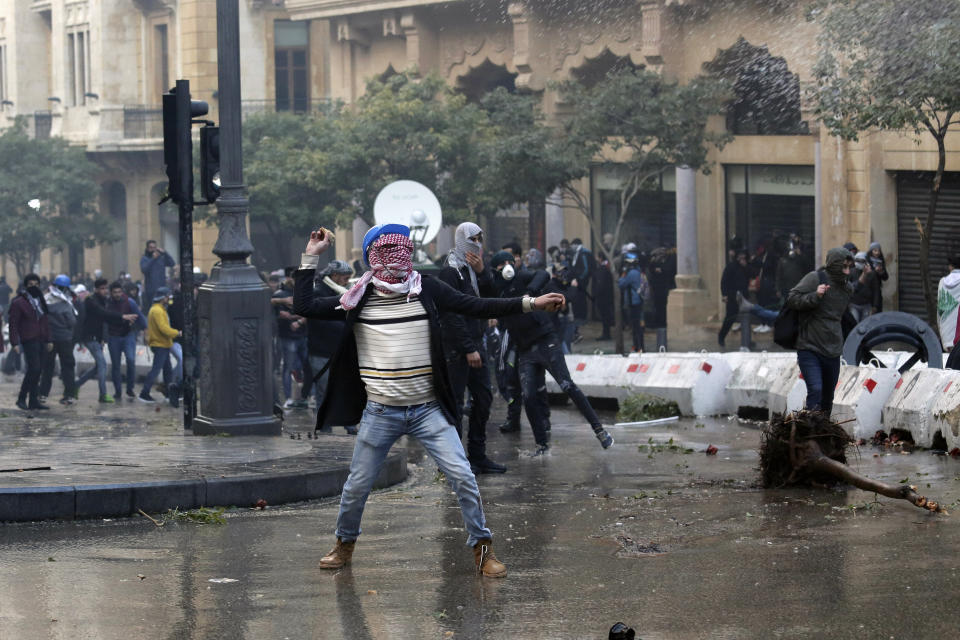 Anti-government demonstrators throw stones toward riot police at a road leading to the parliament building in Beirut, Lebanon, Saturday, Jan. 18, 2020. Riot police fired tears gas and sprayed protesters with water cannons near parliament building to disperse thousands of people after riots broke out during a march against the ruling elite amid a severe economic crisis. (AP Photo/Hassan Ammar)