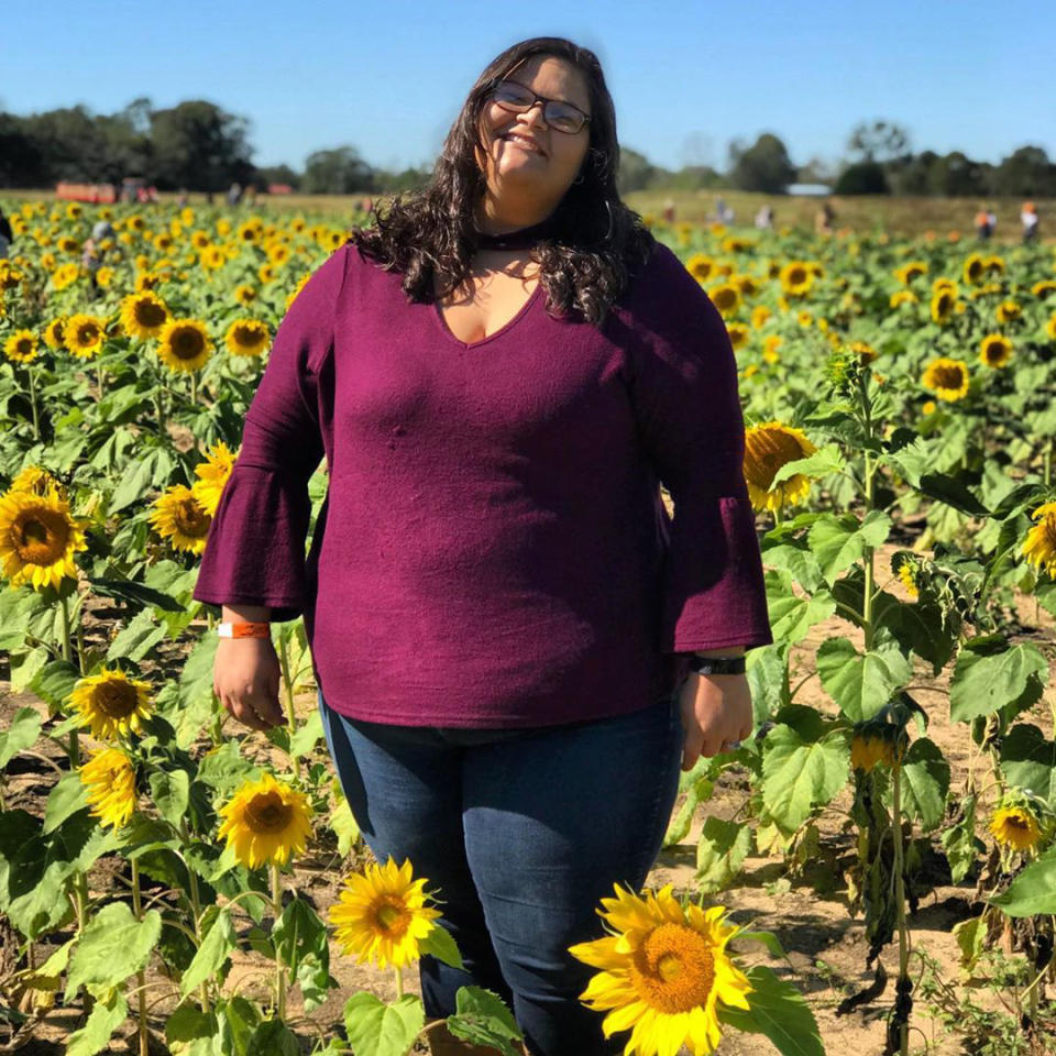 A photo of a woman wearing a purple top standing in a field of sunflowers.