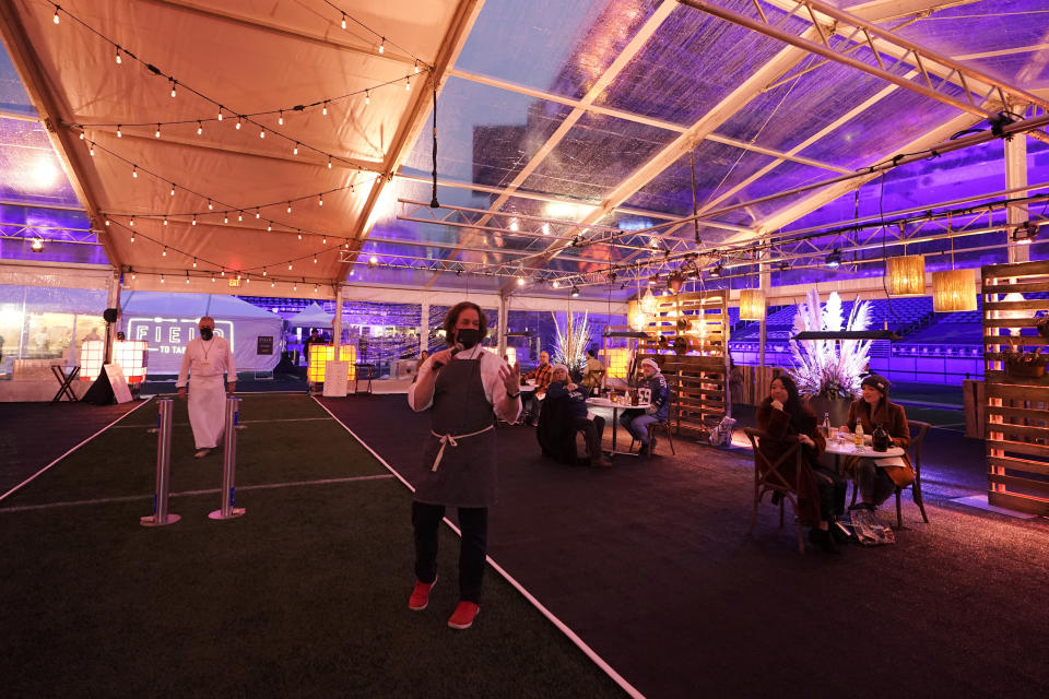 Jason Wilson, center, a chef at The Lakehouse, a restaurant located in Bellevue, Wash., talks about the courses of a meal he prepared with Roy Breiman, left, a chef with Columbia Hospitality, for diners in an outdoor tent set up on the turf at Lumen Field, Thursday, Feb. 18, 2021, in Seattle. Wilson and Breiman were two of the chefs taking part in the inaugural night of the "Field To Table" event at stadium, which is home to the Seattle Seahawks NFL football team. The event will feature several weeks of dates that offer four-course meals cooked by local chefs and served at tables socially distanced as a precaution against the COVID-19 pandemic. (AP Photo/Ted S. Warren)