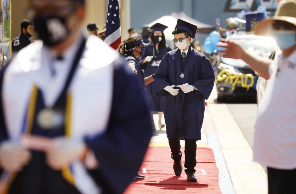 Graduates walk a red carpet to receive their diplomas in a drive-thru graduation ceremony