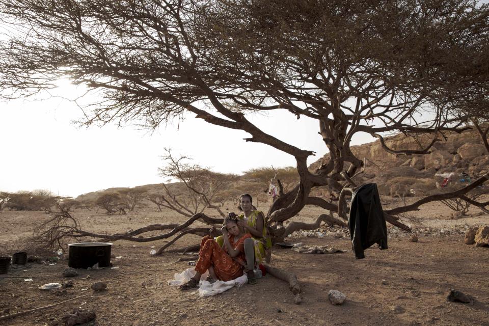 In this July 15, 2019 photo, Fatma, right, a migrant from Ethiopia, braids her friend's hair, as they take shelter on the last stop of their journey before leaving by boat to Yemen in the evening, in Obock, Djibouti. The 100-mile (120-kilometer) trip across Djibouti can take days. Many migrants end up in the country's capital, also named Djibouti, living in slums and working to earn money for the crossing. Young women often are trapped in prostitution or enslaved as servants. (AP Photo/Nariman El-Mofty)