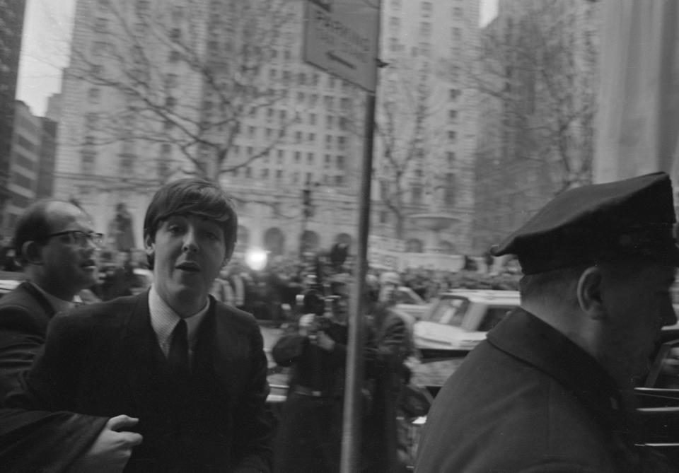 Paul McCartney arrives at a press call in New York. The Beatles are in the USA to appear on the Ed Sullivan TV Show. Police help the band to get into the building through the mass of fans on the street. 8th February 1964. (Photo by Don Smith/Daily Herald/Mirrorpix via Getty Images)