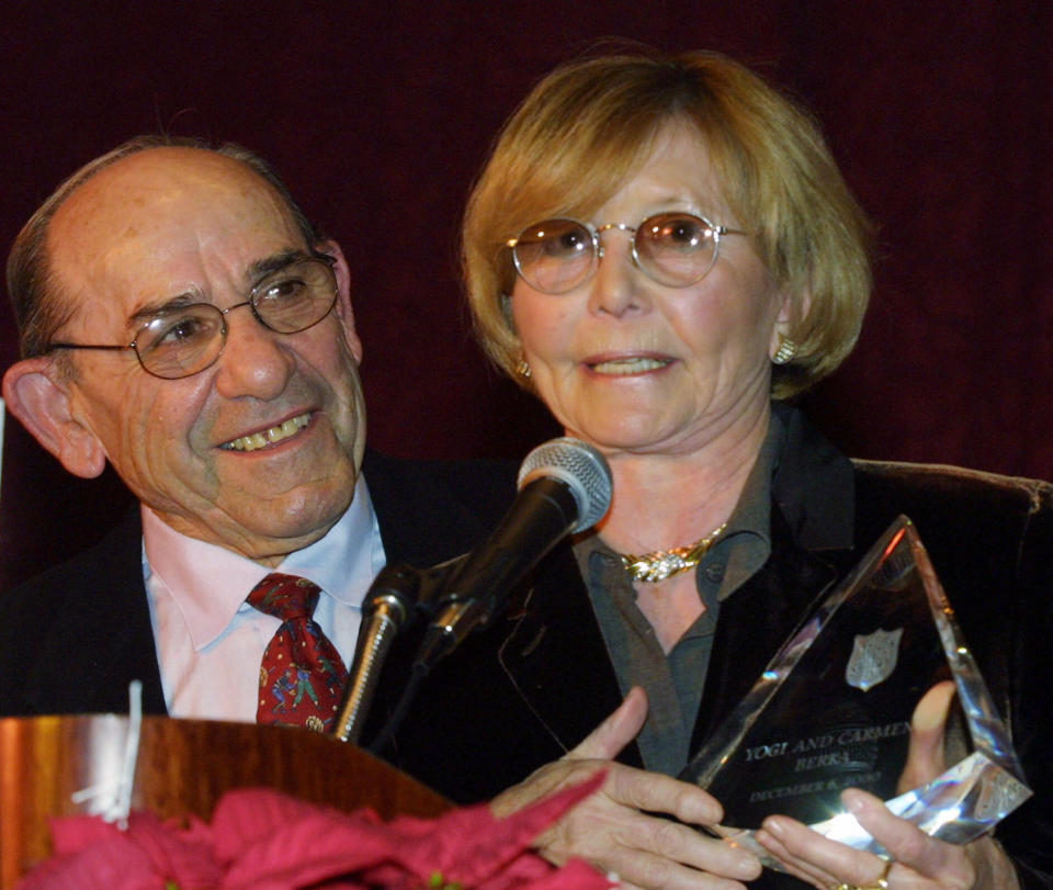 FILE- In this Dec. 6, 2000 file photo, Baseball Hall-of-Famer Yogi Berra listens as his wife Carmen accepts the "Pinnacle of Achievement" award at the Salvation Army Association of Greater New York's Annual Luncheon in New York. According to NJ.com, Dave Kaplan, the director of the Yogi Berra Museum and Learning Center, said that Carmen Berra died of complications from a stroke on Thursday, March 6, 2014. She was 85. (AP Photo/Shawn Baldwin, File)