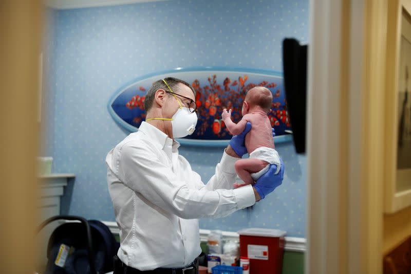 Dr Greg Gulbransen performs a checkup on a young baby as her mother watches while maintaining visits with both his regular patients and those confirmed to have the coronavirus disease (COVID-19) at his pediatric practice in Oyster Bay, New York