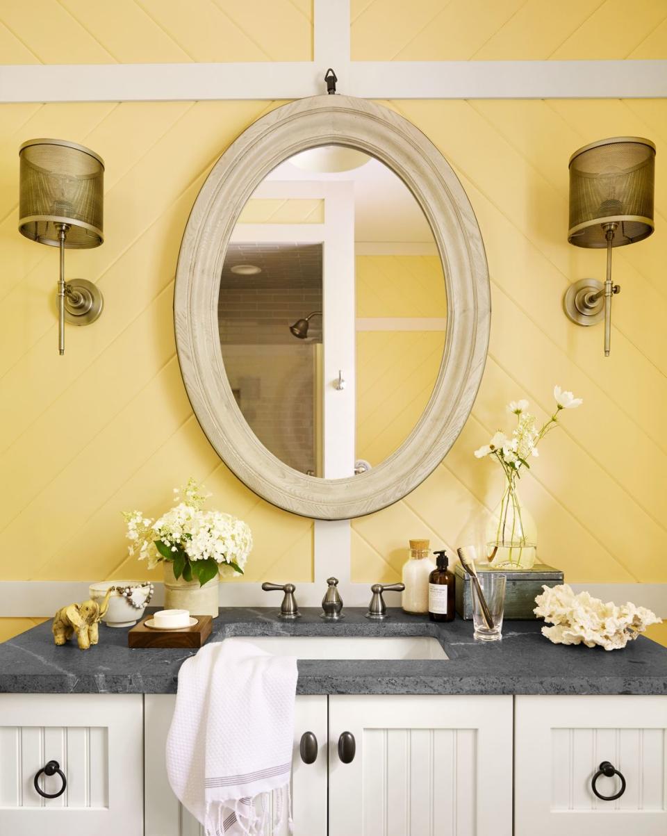 bathroom with paneling painted yellow, white oval mirror, white wood vanity, gray stone countertops