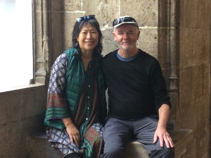May Leong and her husband Rory sitting in front of a stone wall.