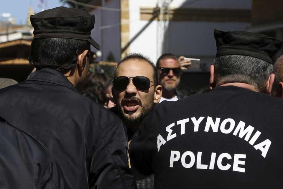 A Turkish Cypriot demonstrator behind the Greek Cypriots riot police, shouts slogans during a protest against a closed crossing point in the ethnically divided capital Nicosia, Cyprus, Saturday, March 8, 2020. Demonstrators staged another protest against a decision by the Cyprus government to temporarily shut four of nine crossing points along a United Nations controlled buffer zone that separates the south from the breakaway Turkish Cypriot north. The Cypriot government says it shut the crossing points to better check for potential coronavirus carriers at the other crossing points. (AP Photo/Petros Karadjias)