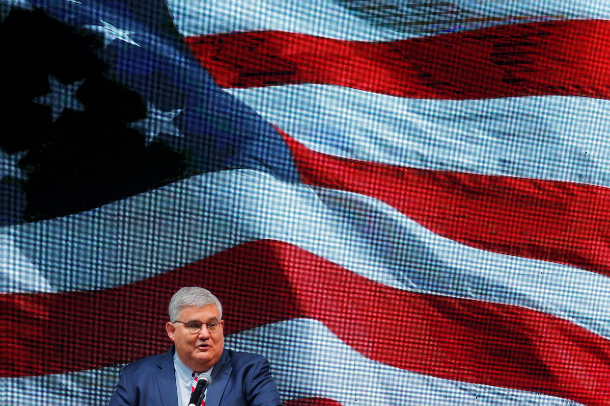 David Shafer in front of a huge image of a billowing American flag.