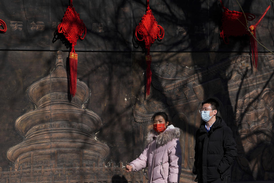 Residents wearing face masks to help protect from the coronavirus walk by a mural decorated with Lunar New Year decorations in Beijing, Tuesday, Feb. 8, 2022. China has ordered inhabitants of the southern city of Baise to stay home and suspended transportation links amid a surge in COVID-19 cases at least partly linked to the omicron variant. (AP Photo/Andy Wong)