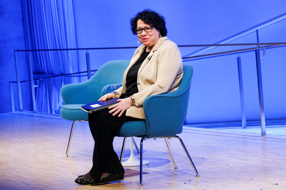 Supreme Court Justice Sonia Sotomayor sits onstage in a chair with folders on her lap.