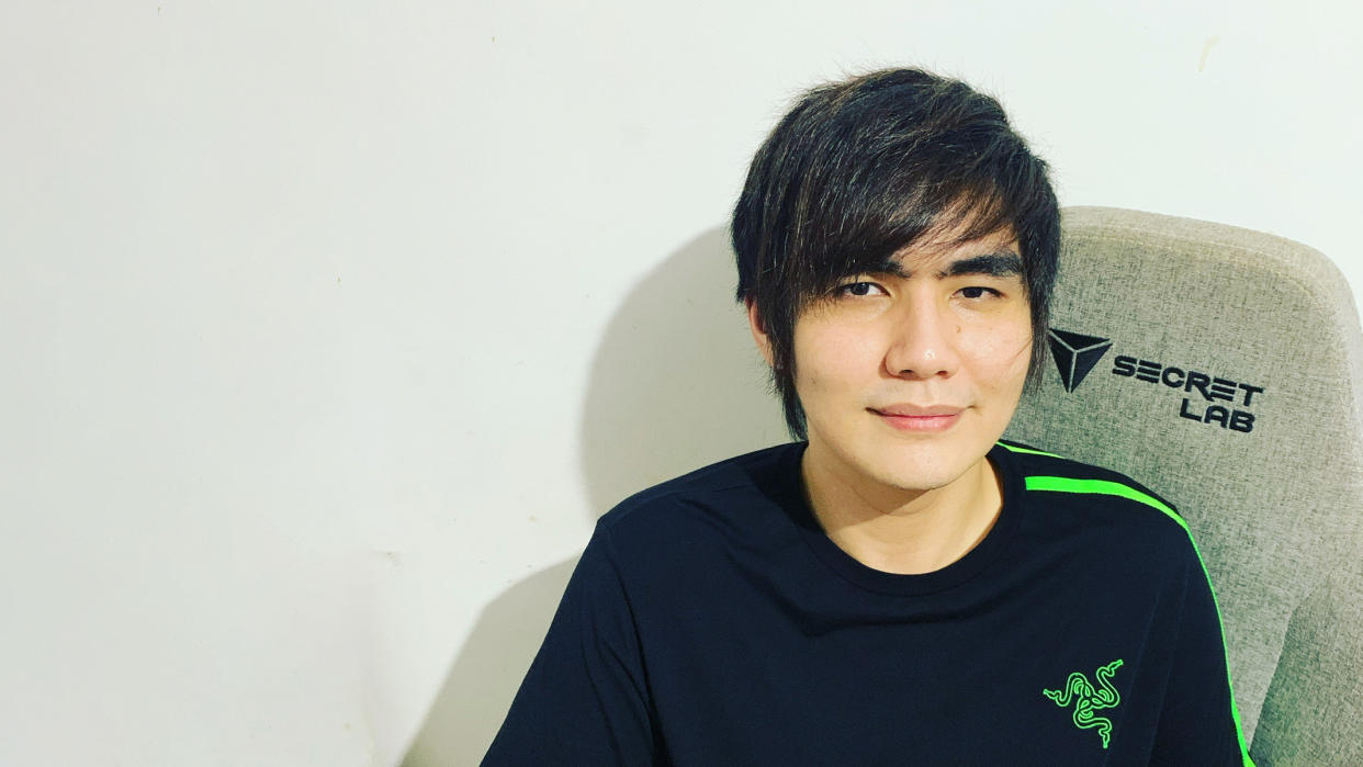 A picture of Singaporean Street Fighter player, Xian, in a Razer shirt, sitting on a grey Secret Lab chair.