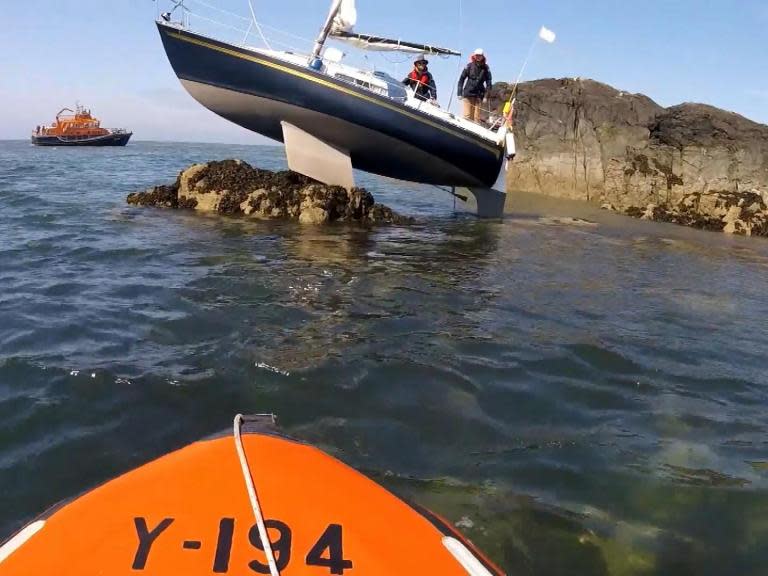 Footage has been released showing two people being rescued after their 25-foot yacht was stranded on rocks off the coast of Anglesey.Volunteers from the RNLI" data-wsc-lang="en_GB">Holyhead Royal National Lifeboat Institution (RNLI) were called on Sunday afternoon, making their way out to the pair just before 2pm. A low tide meant the vessel couldn’t be moved immediately, and it had to be temporarily abandoned, but the people on board were brought to safety. Both appeared to be unharmed.Video recorded by the RNLI shows the moment they were discovered, with the yacht’s keel wedged up onto a small island, one of the team shouting to ask if they are okay.The lifeboat team can then be seen returning to the boat that evening, five hours later, once the tide had risen again. After it eventually became dislodged, the team then tugged it back into the harbour.