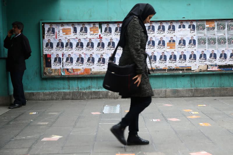 A woman walks past parliamentary election campaign posters in Tehran