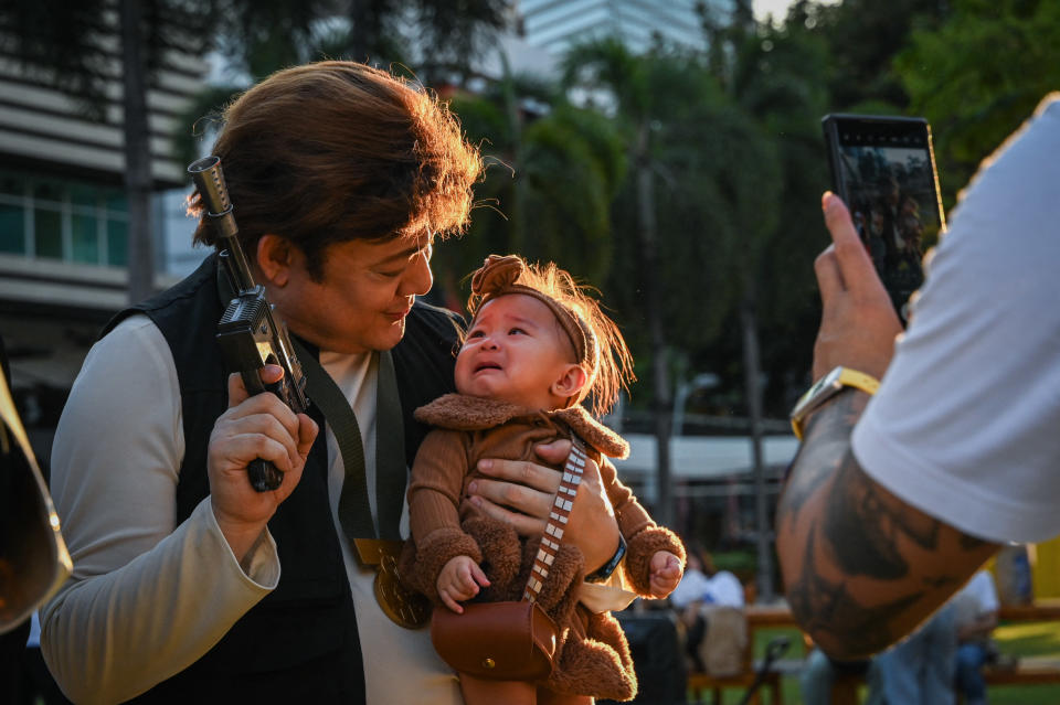 A Star Wars fan in Manila holds a fake gun and a baby in costume.
