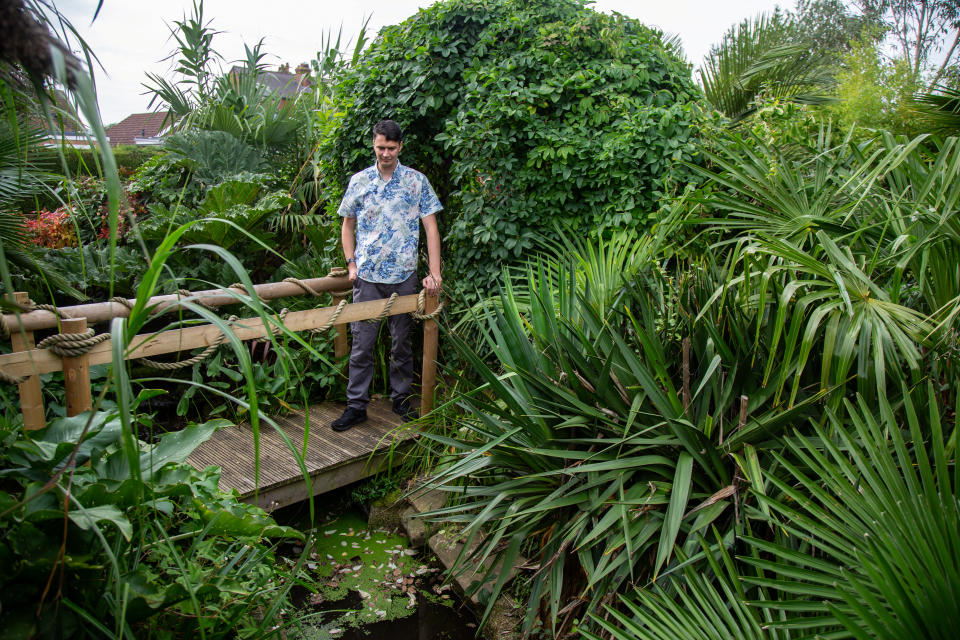 Kris Swaine standing on a wooden footbridge above a rock waterfall. (SWNS)